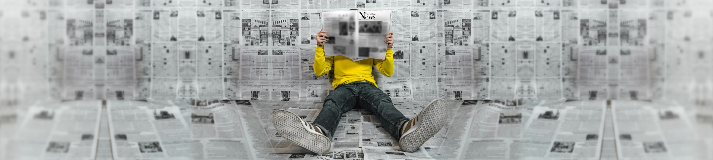 Someone sitting against a wall of newspapers, reading The Village News